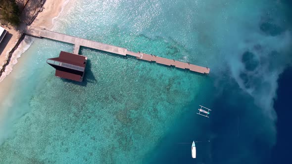 Epic aerial top down of crystal clear coral reefs under wooden pier on Gili Meno Island during sunsh