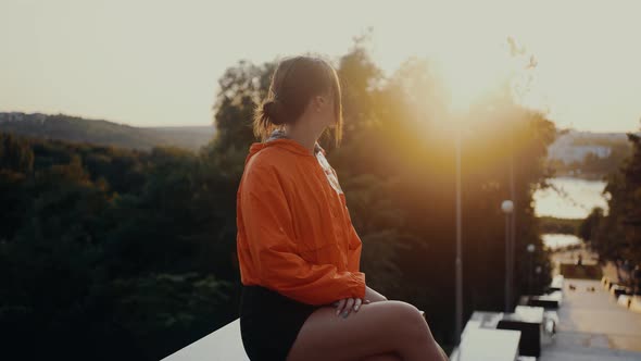 The Young Redhead in a Bright Orange Blouse is Sitting in the Park and Admires the View That