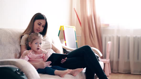 Travelling  Young Attractive Mother and Sweet Daughter Are Sitting on the Couch