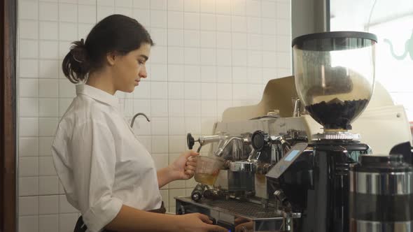 Close up of woman worker, barista in apron making a coffee by using coffee machine in kitchen bar