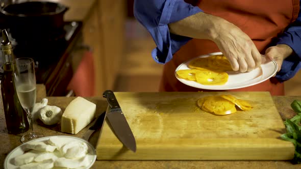 Chef takes freshly cut yellow heirloom tomato slices and arranges them on a plate and then sprinkles