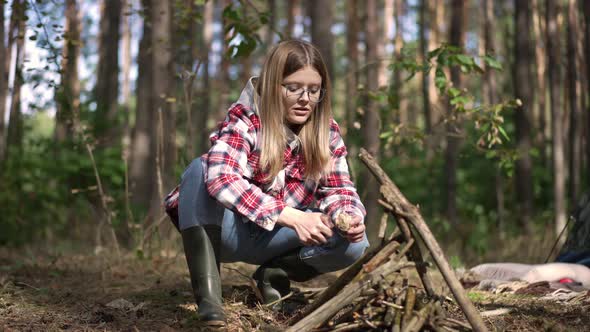 Attractive Young Female Tourist Setting Fire in Forest Sitting at Tent Outdoors