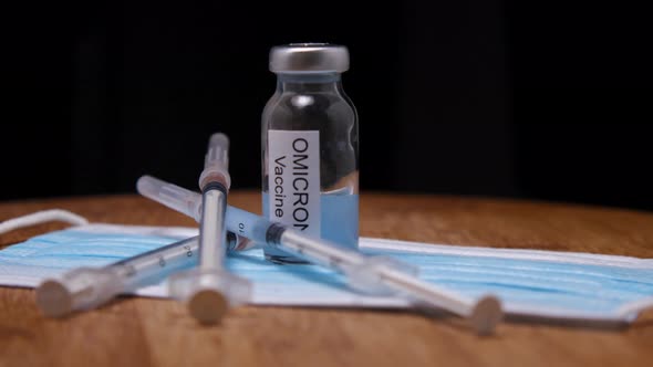 Medical mask, syringes and vial of Omicron vaccine on wooden background. The camera flies around