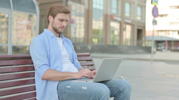 Man with Laptop Smiling at Camera While Sitting Outdoor on Bench