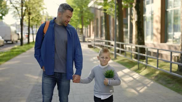 Father Carrying Backpack Holding Son's Hand and Son is Holding the Plant in a Pot After Ecology