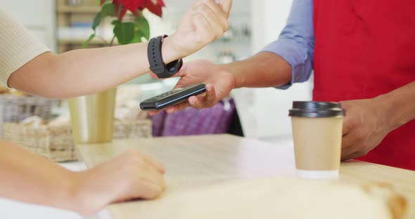 Video of hands of biracial woman paying with smartwatch for baguette