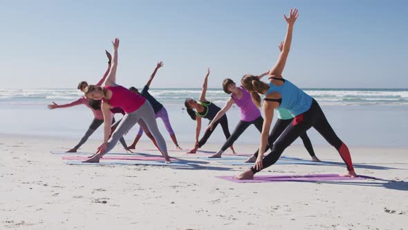 Multi-ethnic group of women doing yoga position on the beach and blue sky background