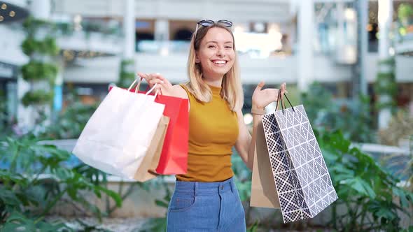 cheerful young shopaholic woman holding paper bags with purchases and smiling looking at camera 