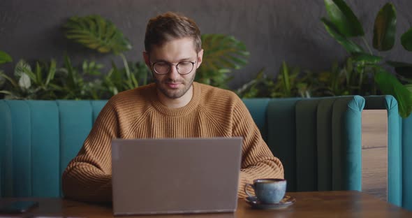 Adult Man Sits in Cafe in Daytime and Using the Laptop for the Remote Work