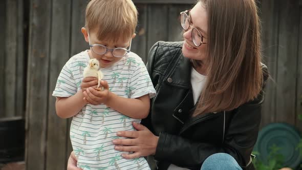 Child and Mother Holding a Chick in Hand in Backyard of Farm