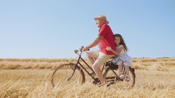 Little Girl Holds on to Grandpa Riding Bicycle in Field