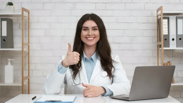 Female Doctor Gesturing Thumbs Up Posing At Workplace Indoor