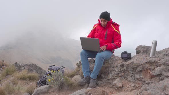 Young latin man working with laptop computer in the rock with mountain scenic view, ​digital nomad o