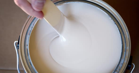 Hand stirring white paint with wooden stick