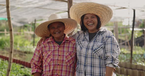 Happy Asian woman farmers looking to camera and laughing together on local organic vegetable farm.