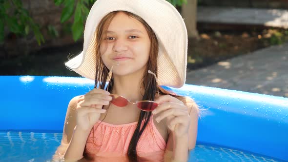 Beautiful Msiling Teenage Girl Relaxing in Swimming Pool and Taking Off Sunglasses