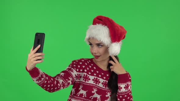 Portrait of Sweety Girl in Santa Claus Hat Is Making Selfie on Mobile Phone Then Looking Photos