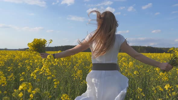 A Girl in a White Dress Runs Among a Rapeseed Field alt