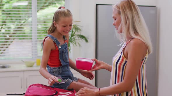 Caucasian mother in kitchen preparing packed lunch and talking with daughter