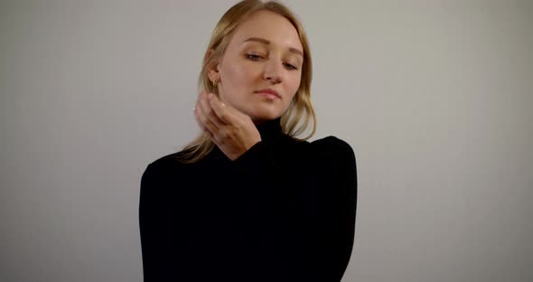 Graceful Blonde Woman Is Moving Hand and Smiling, Standing on White Wall Background