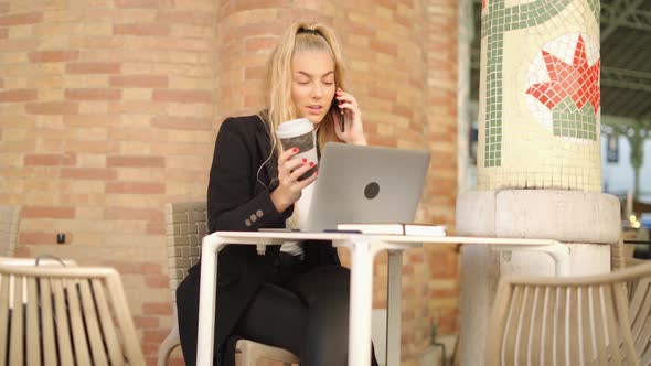 Woman talking on smartphone while working with laptop in cafe