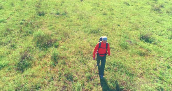 Flight Over Backpack Hiking Tourist Walking Across Green Mountain Field. Huge Rural Valley at Summer