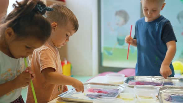 Multiethnic Group of Toddlers Milk Painting with the Teacher Helping Them Using Food Coloring for