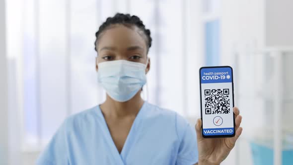 Young Afroamerican Doctor in Medical Mask Showing Smartphone in Her Hand with Mobile Application for