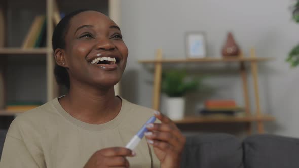 Smiling Woman Sitting on Sofa with Pregnancy Test in Hands