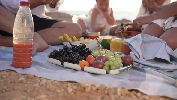 Fruits in Sunshine on Picnic Blanket with Unrecognizable Caucasian Tanned Family Enjoying Leisure on