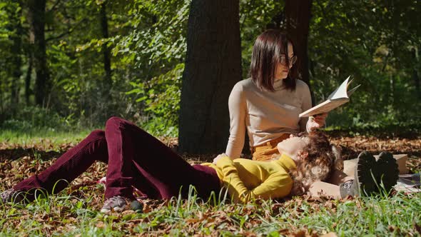 Two Happy Young Women Have Fun Sitting in the City Park