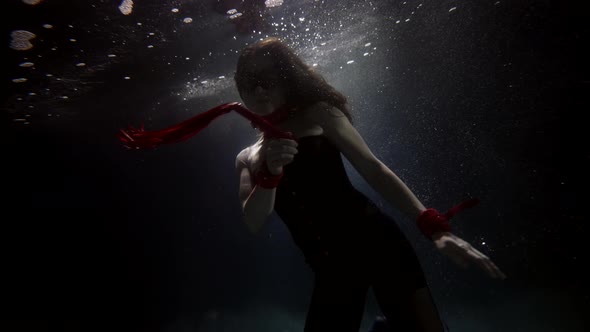 Magic Underwater Shot of Slim Woman Floating in Dark Depth Figure in Darkness Holding Red Whip
