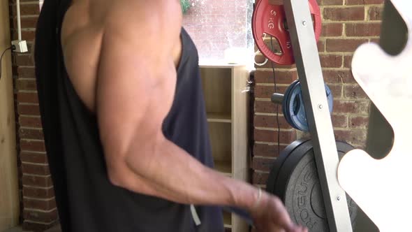 Muscly man in home gym exercising bicep curl barbell smith machine