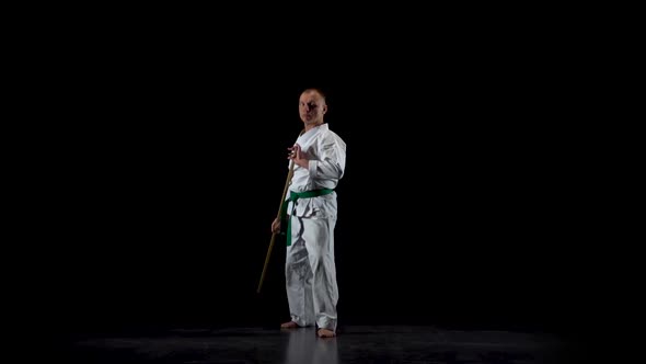 Kendo Fighter on White Kimono Practicing Martial Art with the Bamboo Bokken on Black Background