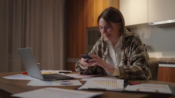 Happy Woman Using Mobile Phone While Working at Home with Laptop