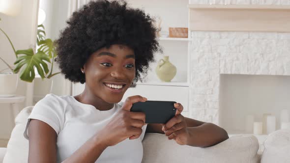 Happy Relaxed Millennial Mixed Race Girl Holding Smartphone Looking at Cellphone Screen Laughing