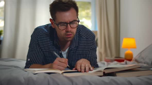 College Student Lying on Bed at Home and Writing in Copybook and Reading Books When Doing Homework