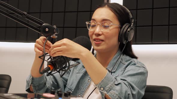 Brunette young Asian woman talking into microphone while recording radio show