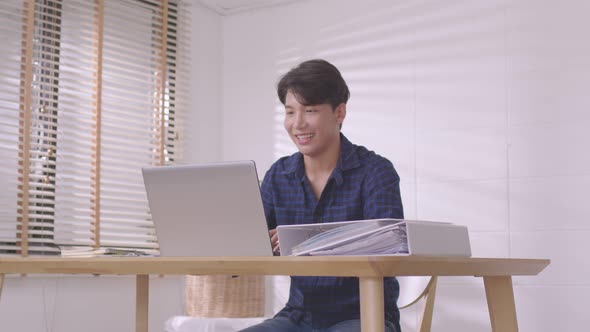 At home, a business asian man types and works online on a desk table with a laptop.