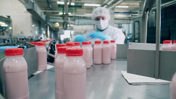 Factory Worker Picks Yogurt Bottles From a Moving Line.
