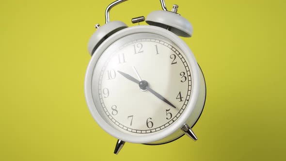Classic analog alarm clock with bells rotates on a colored yellow background