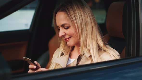 The Woman Driver Is Sitting Behind the Steering Wheel Reading a Text Message on a Mobile