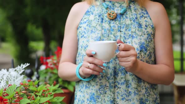 Woman in a Summer Cafe Pours Tea Into a Cup Close-up Standing. Woman Stands on the Background of the