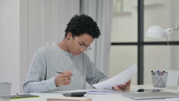 African Woman Using Calculator While Writing on Paper