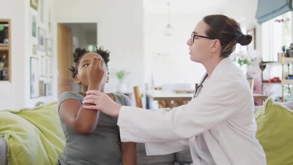 African american girl and caucasian female doctor sitting on sofa in living room using inhaler