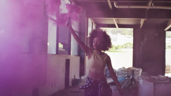 Mixed race woman holding purple flare running through an empty building