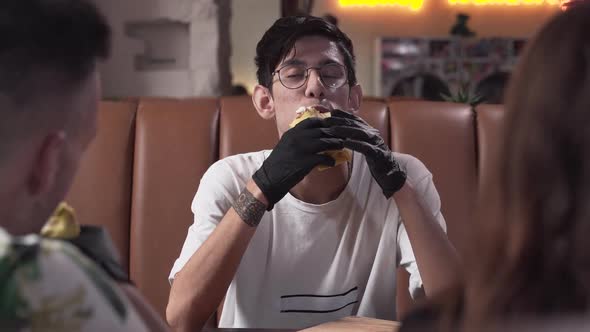 Cute Skinny Young Man in Glasses and Black Gloves Eating Tasty Shawarma