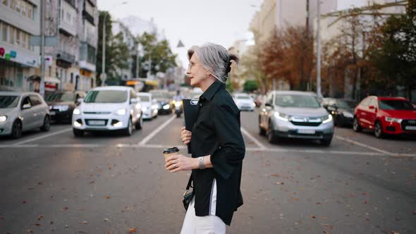 Active Adult Woman Crosses the Street at an Intersection Opposite to the Cars Standing in a Row