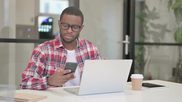 African Man Using Smartphone While Using Laptop