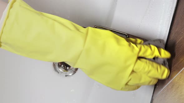 Close up of woman in gloves wipes sink and washbasin. House cleaning concept.